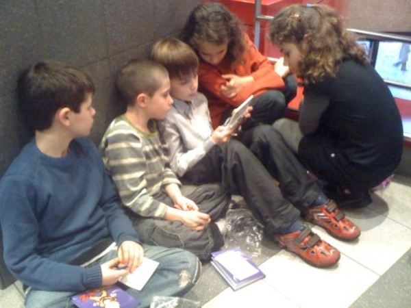 Photo d'enfants agglutinés autours d'une console de jeu portable.